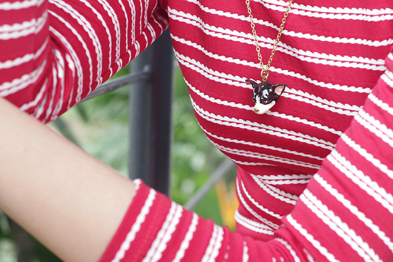 A close-up of a cute dog necklace worn on a red striped shirt.