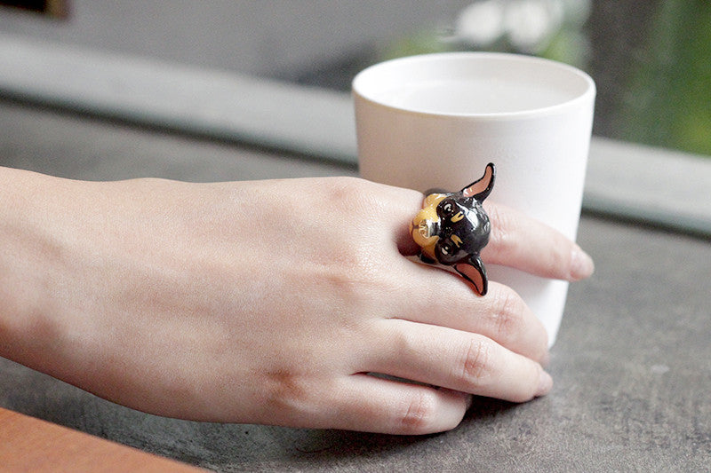 A hand wearing a cute dog ring while holding a cup.