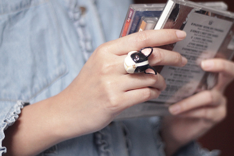 A hand holding CDs with a cute French Bulldog ring on the finger.