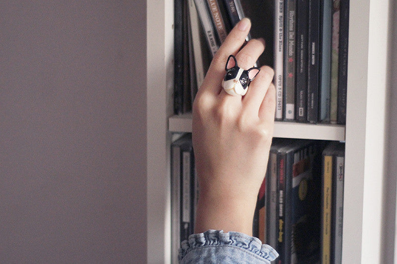 Close-up of a unique dog ring on a hand next to a shelf of CDs.