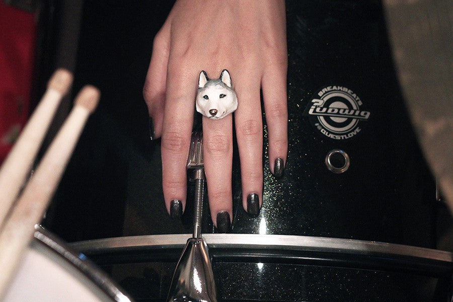 A hand with a Siberian husky ring rests on a black drum, with drumsticks positioned nearby.