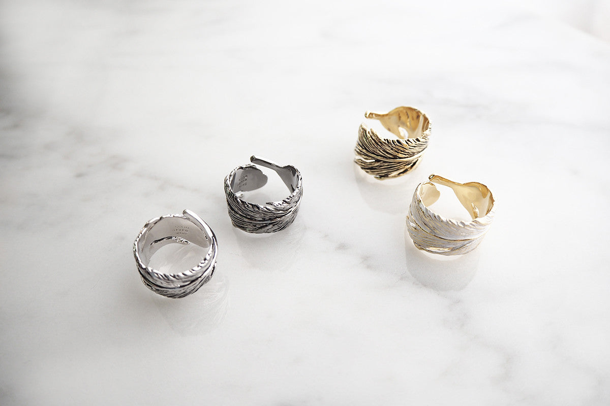 Stylish rings with feather patterns in silver and gold on a marble table.