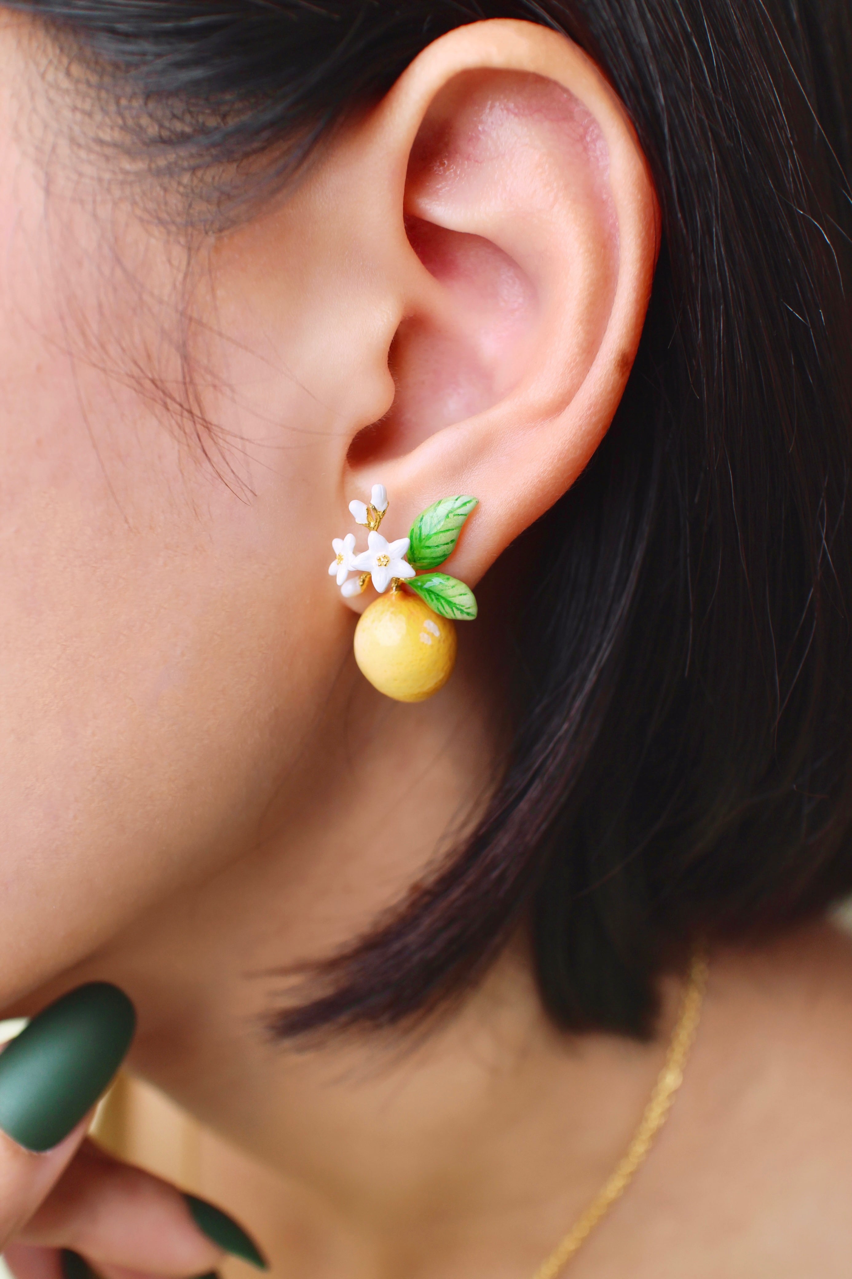 A close-up of an ear wearing charming lemon earrings adorned with white flowers and green leaves.