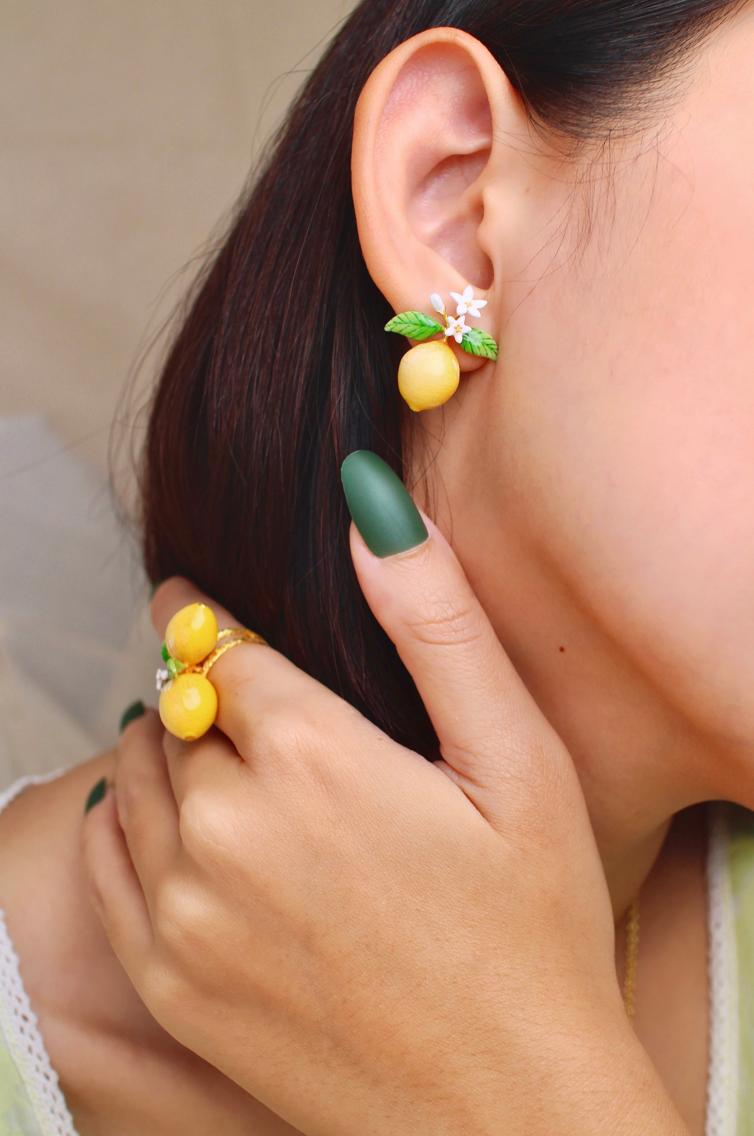 A close-up of a woman wearing charming lemon earrings and a matching ring