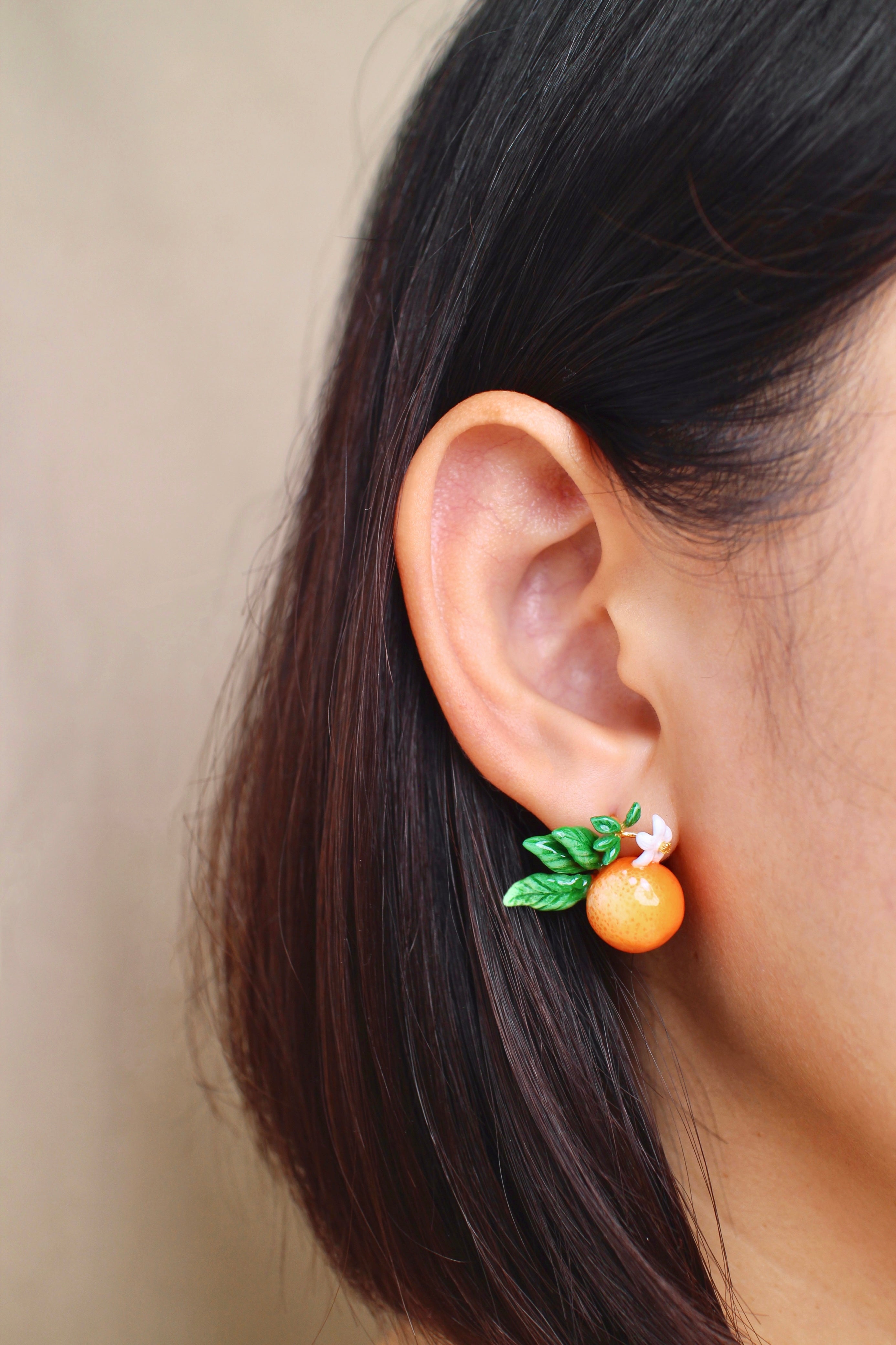 A close-up of an ear wearing orange earrings adorned with white flowers and green leaves.