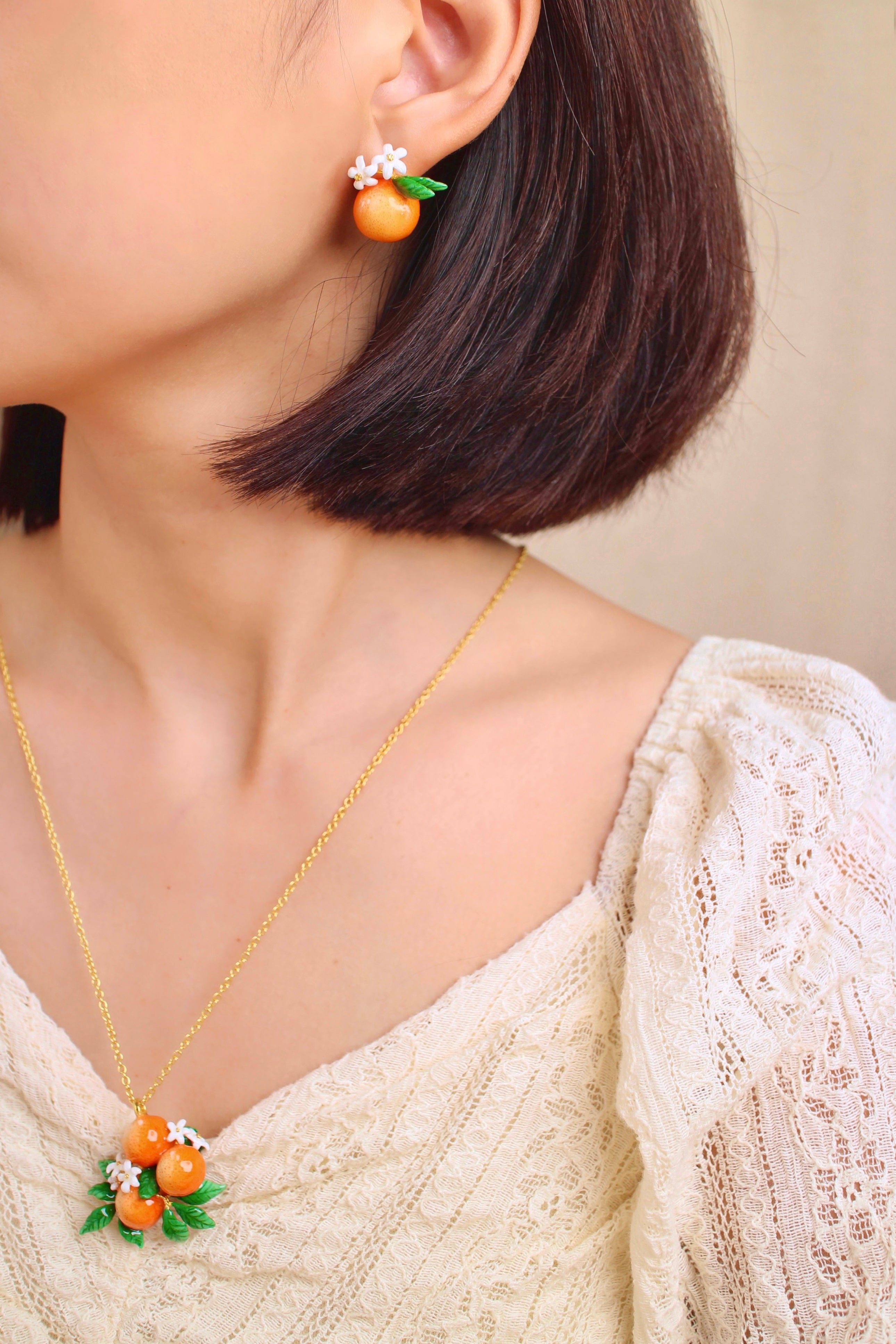 A close-up of a woman wearing beautiful orange earrings and an orange pendent necklace.