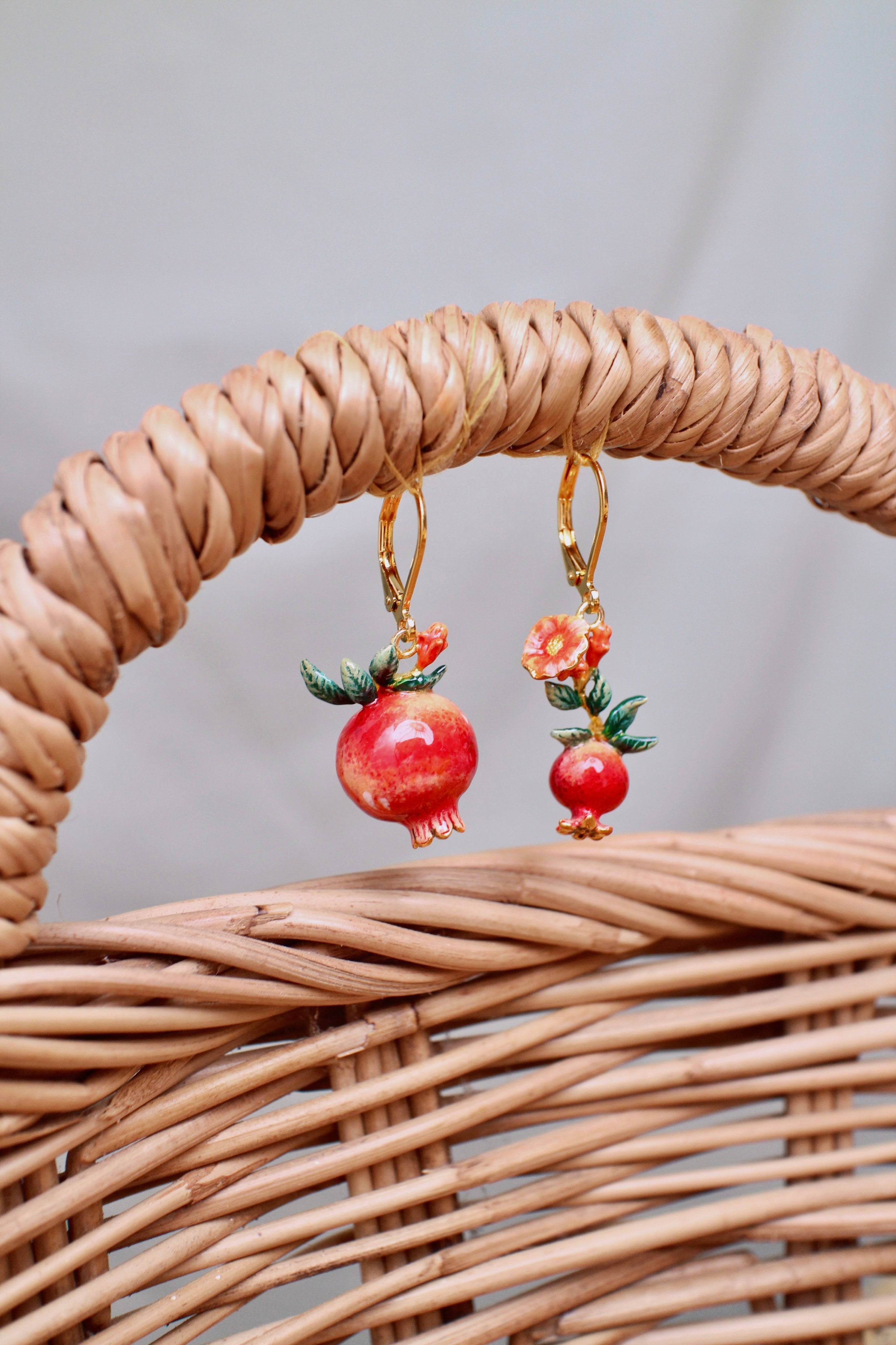 Close-up of beautiful pomegranate earrings adorned with delicate red flowers and green leaves hanging with a handle wicker basket