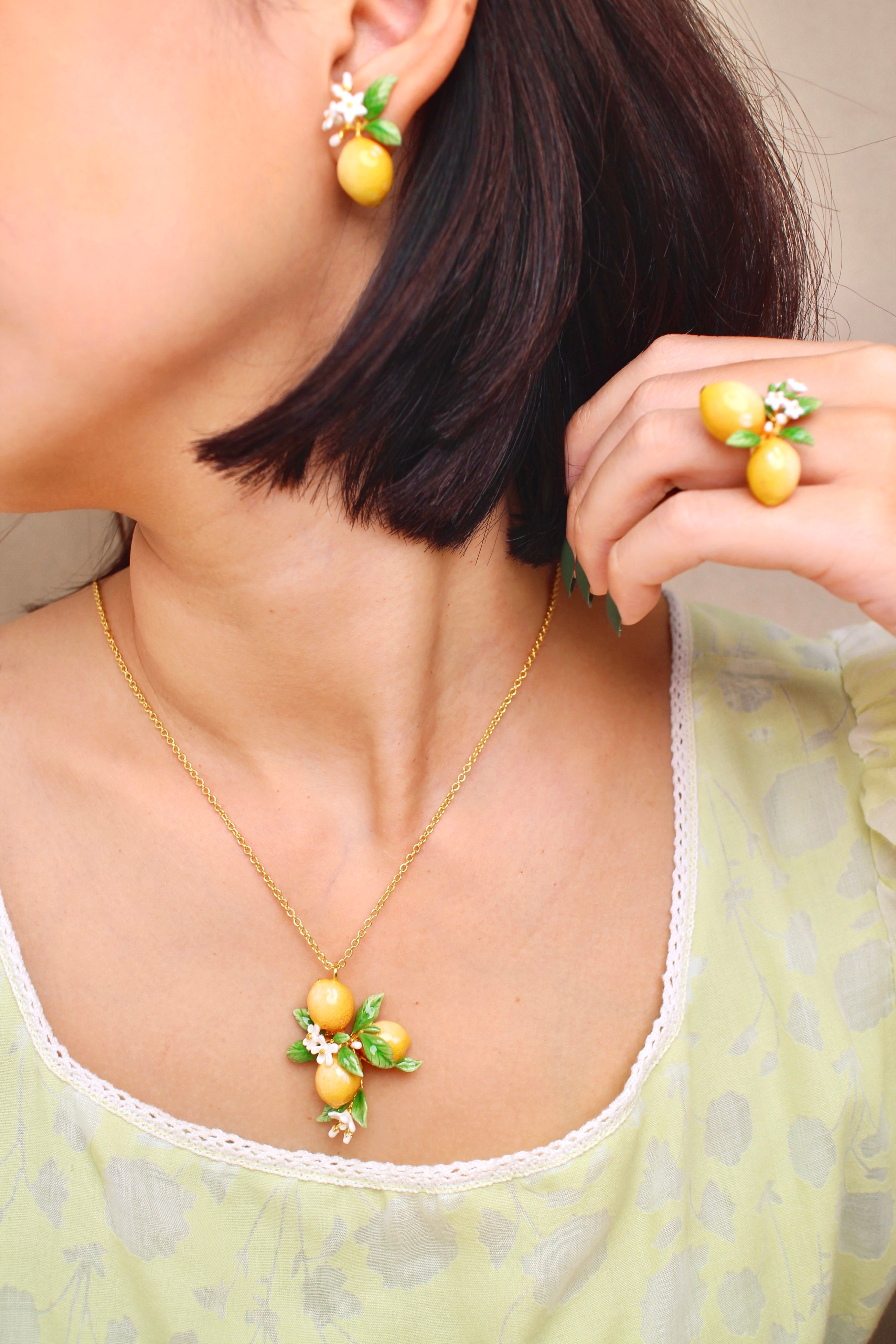 A woman wears a lemon-themed jewelry set, including earrings, a necklace, and a ring, in a summer outfit.