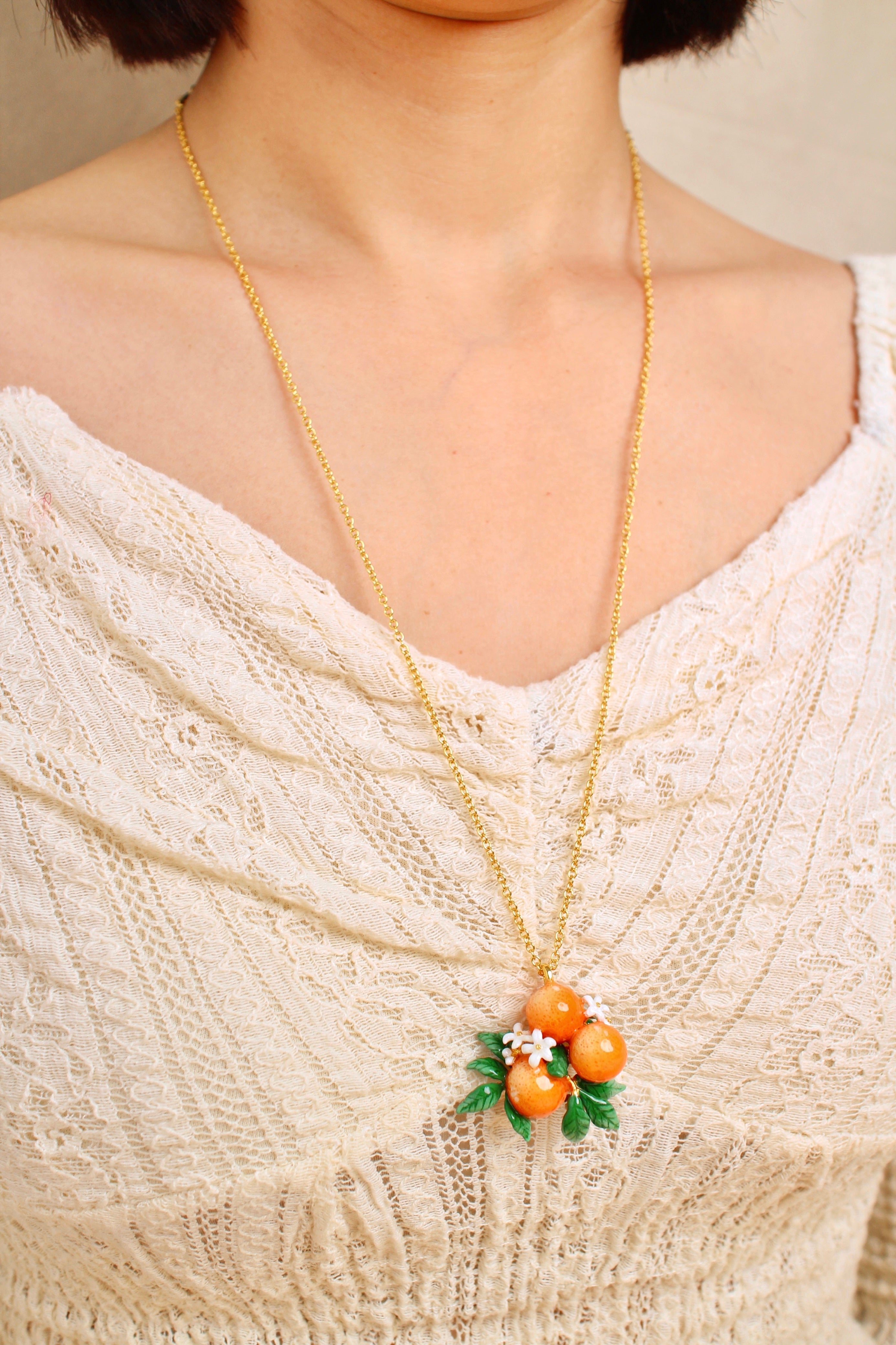 A close-up of a person wearing a gold chain necklace with orange charm and white flower accents, in a summer outfit.