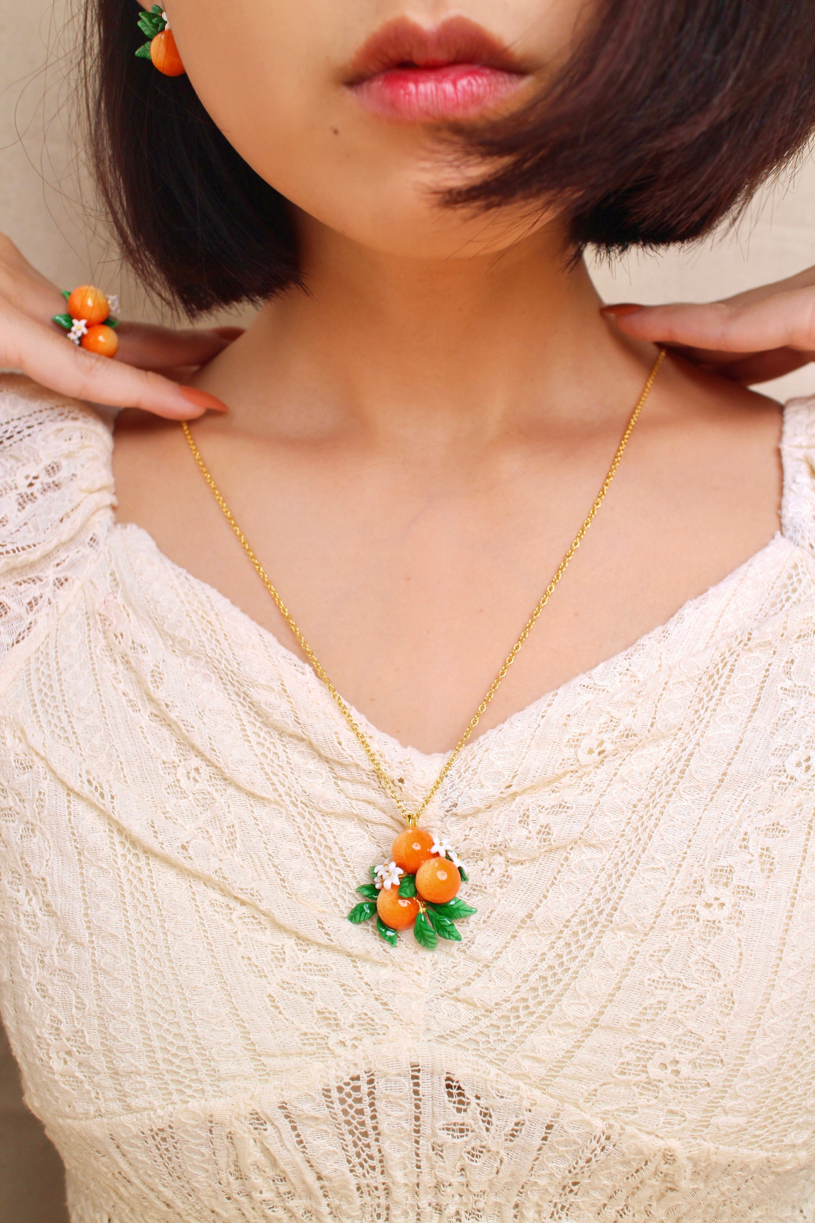 A woman wears a orange-themed jewelry set, including earrings, a necklace, and a ring, in a summer outfit.