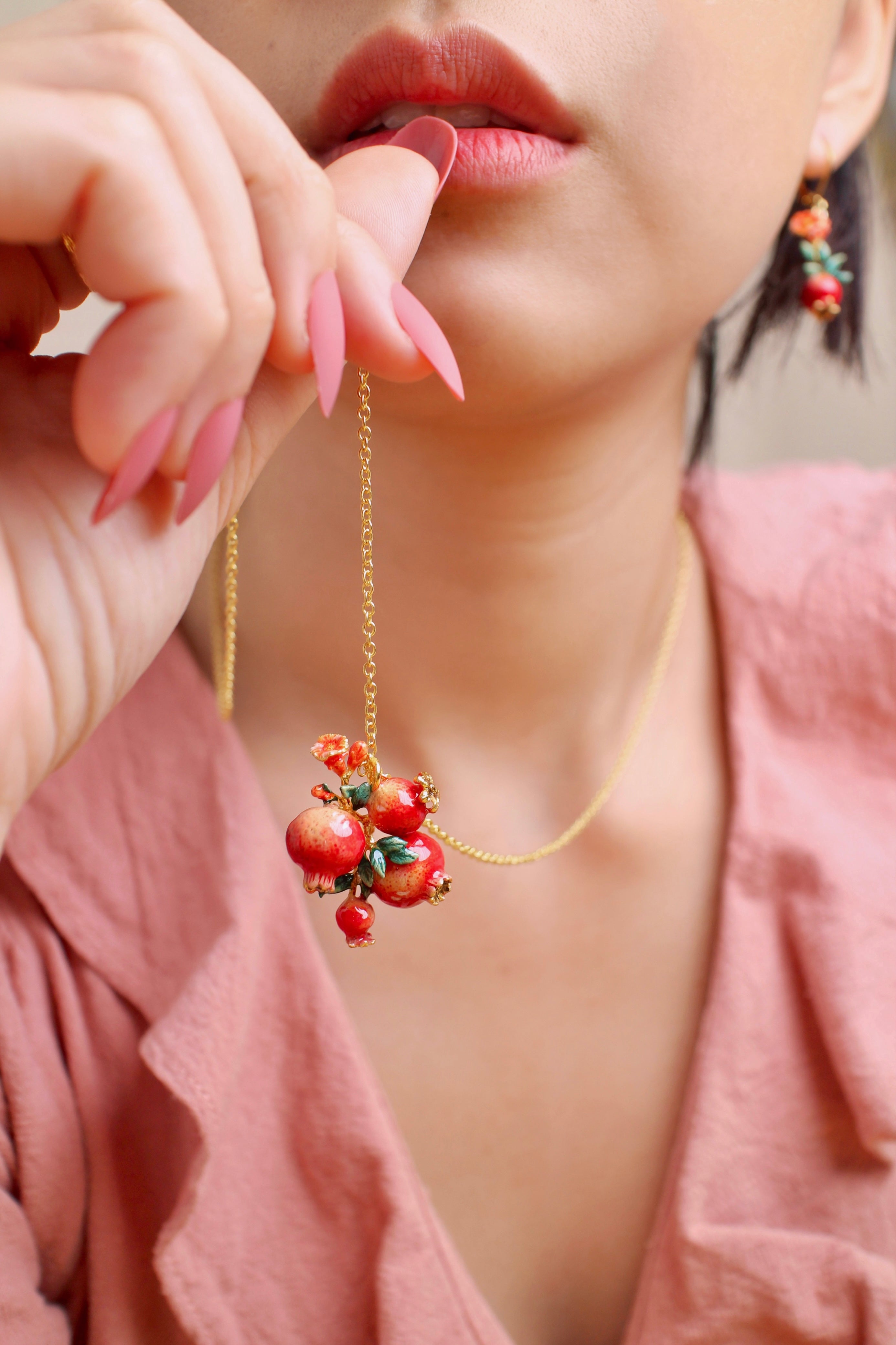 A woman wears a pomegranate-themed jewelry set, including a necklace and earrings, in a summer outfit.