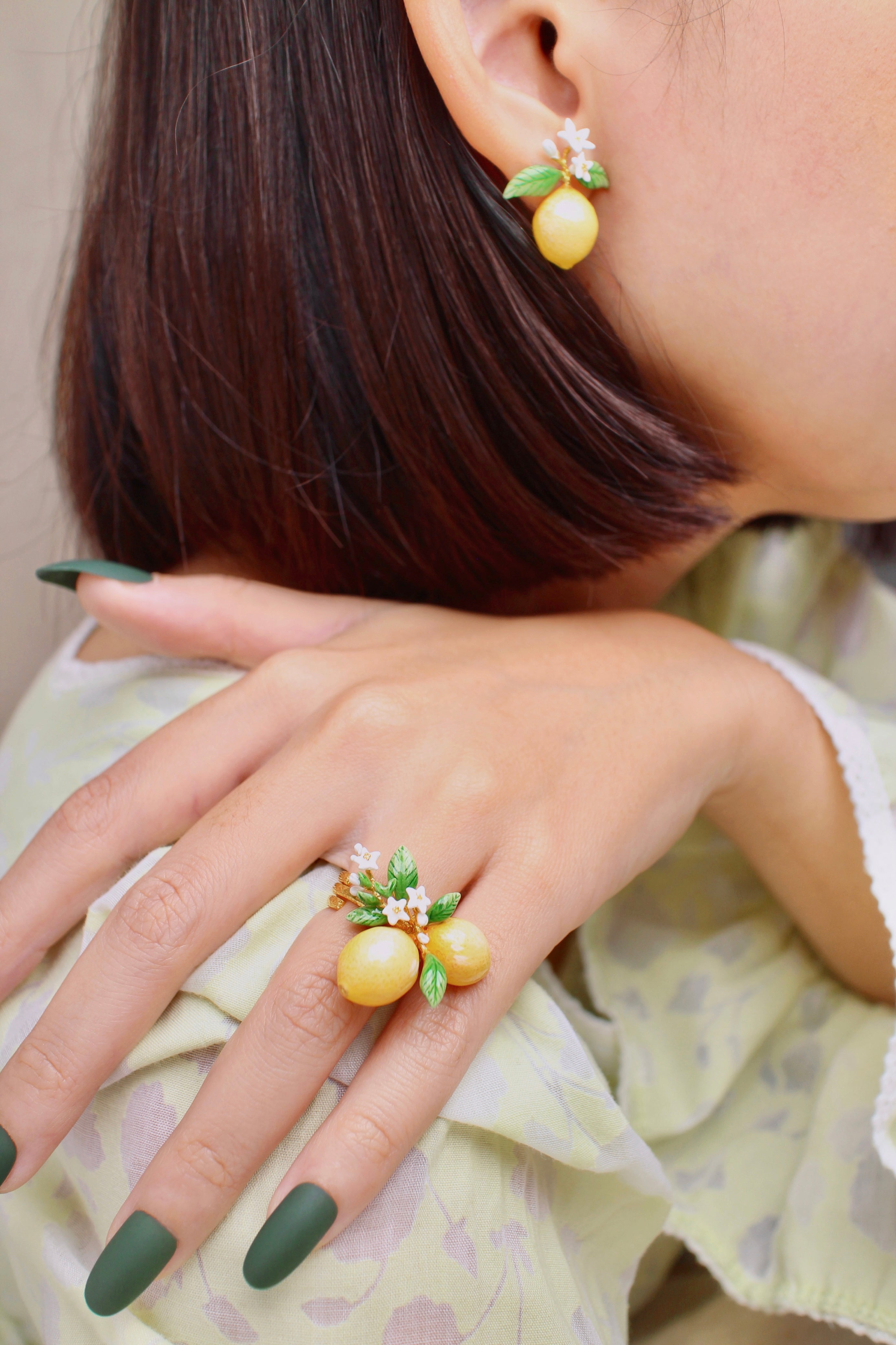 A woman wears a lemon-themed jewelry set, including earrings and a ring, in a summer outfit.