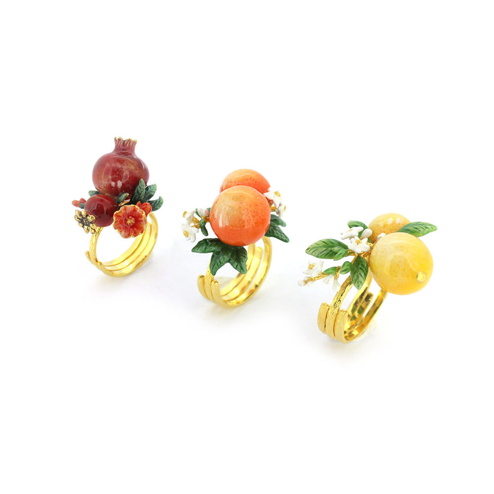 Three stunning rings featuring colorful fruit designs: a pomegranate, orange, and lemon, all set on gold bands.