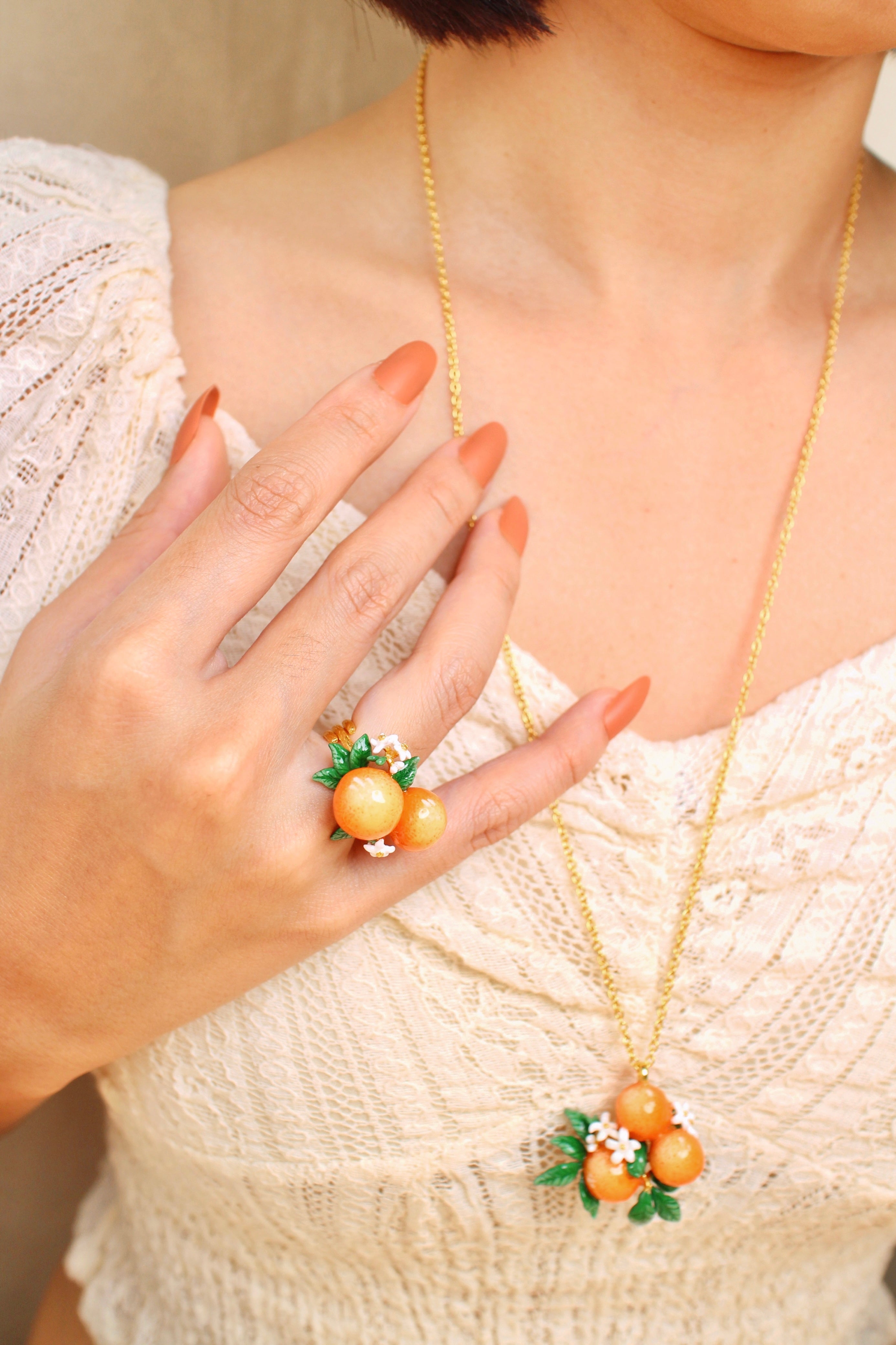 A woman wears a orange-themed jewelry set, including a necklace and a ring, in a summer outfit.