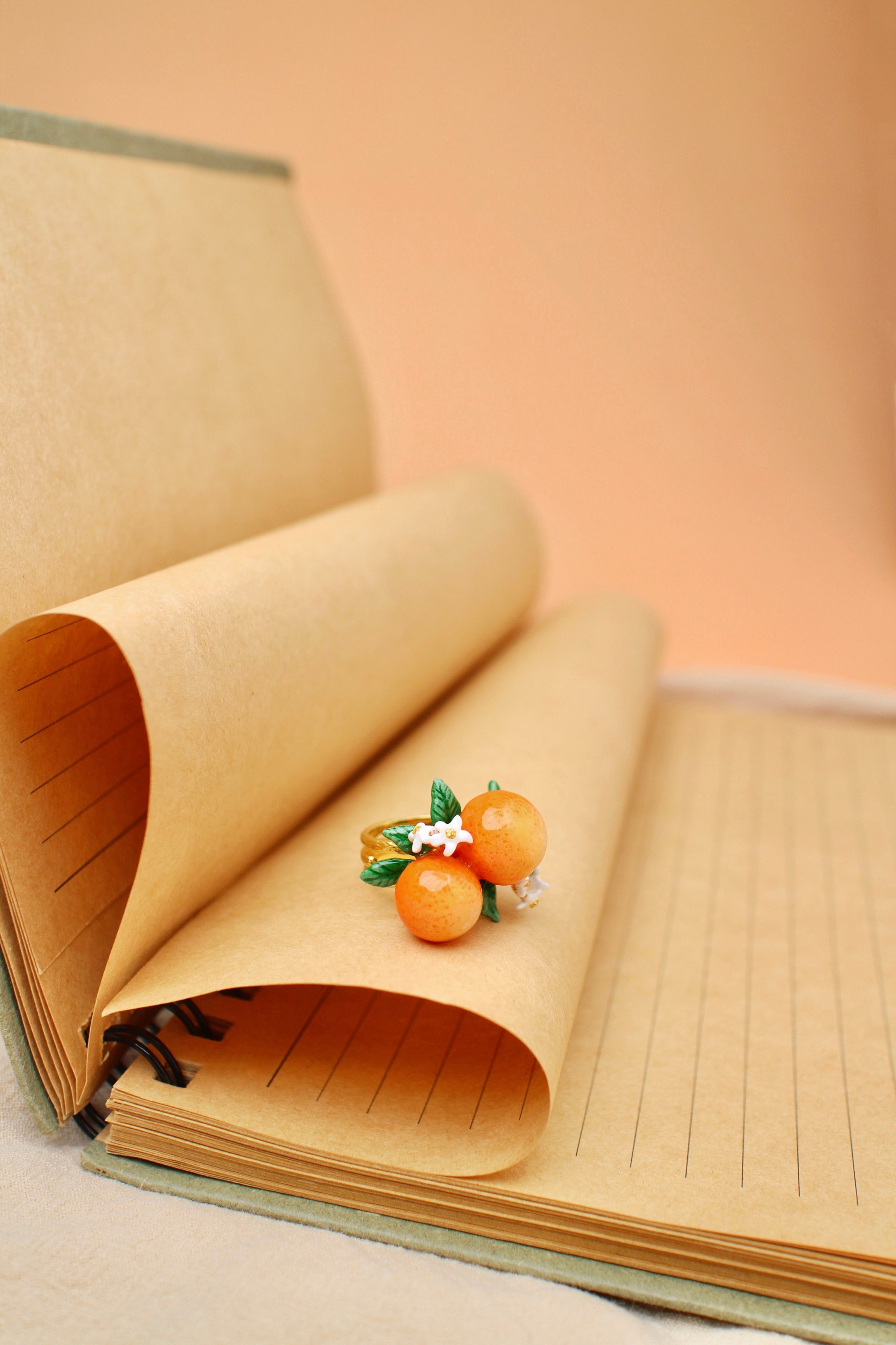 A stunning gold ring featuring two oranges, green leaves, and small white flowers, placed on brown paper.