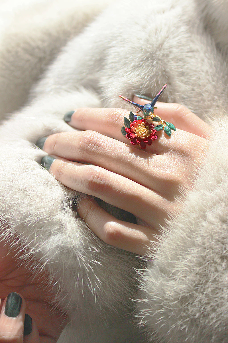 rtistic ring design featuring a bird and flower, shown on a hand with fur fabric.