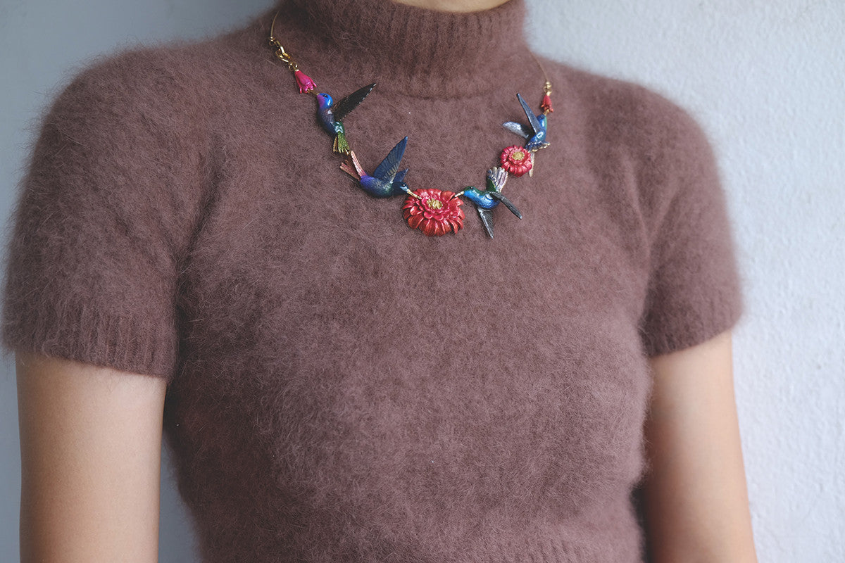 An elegant necklace adorned with hummingbird and flower designs, paired with a fuzzy brown sweater.