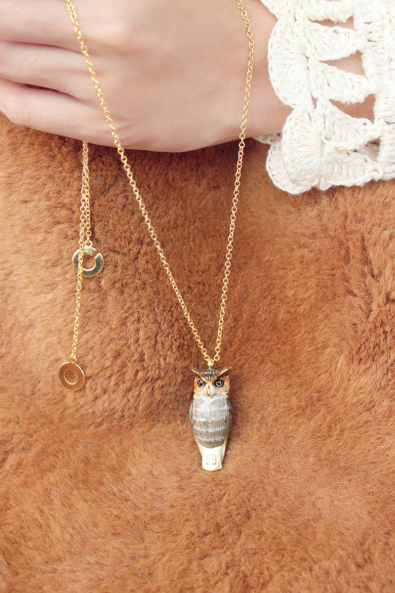 A whimsical owl whistle necklace with a gold chain a on a person's hand.