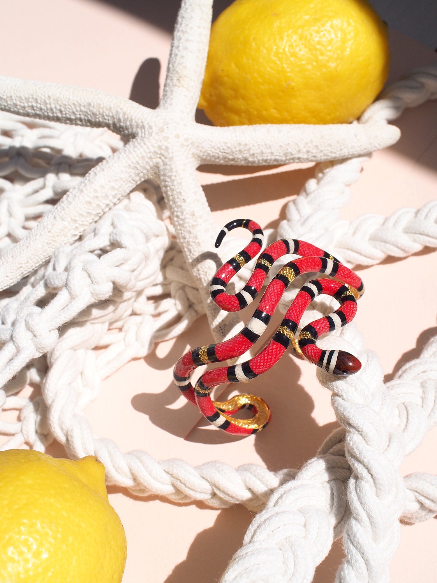 A striking red snake bangle place on a soft pastel background with decorative summer elements.