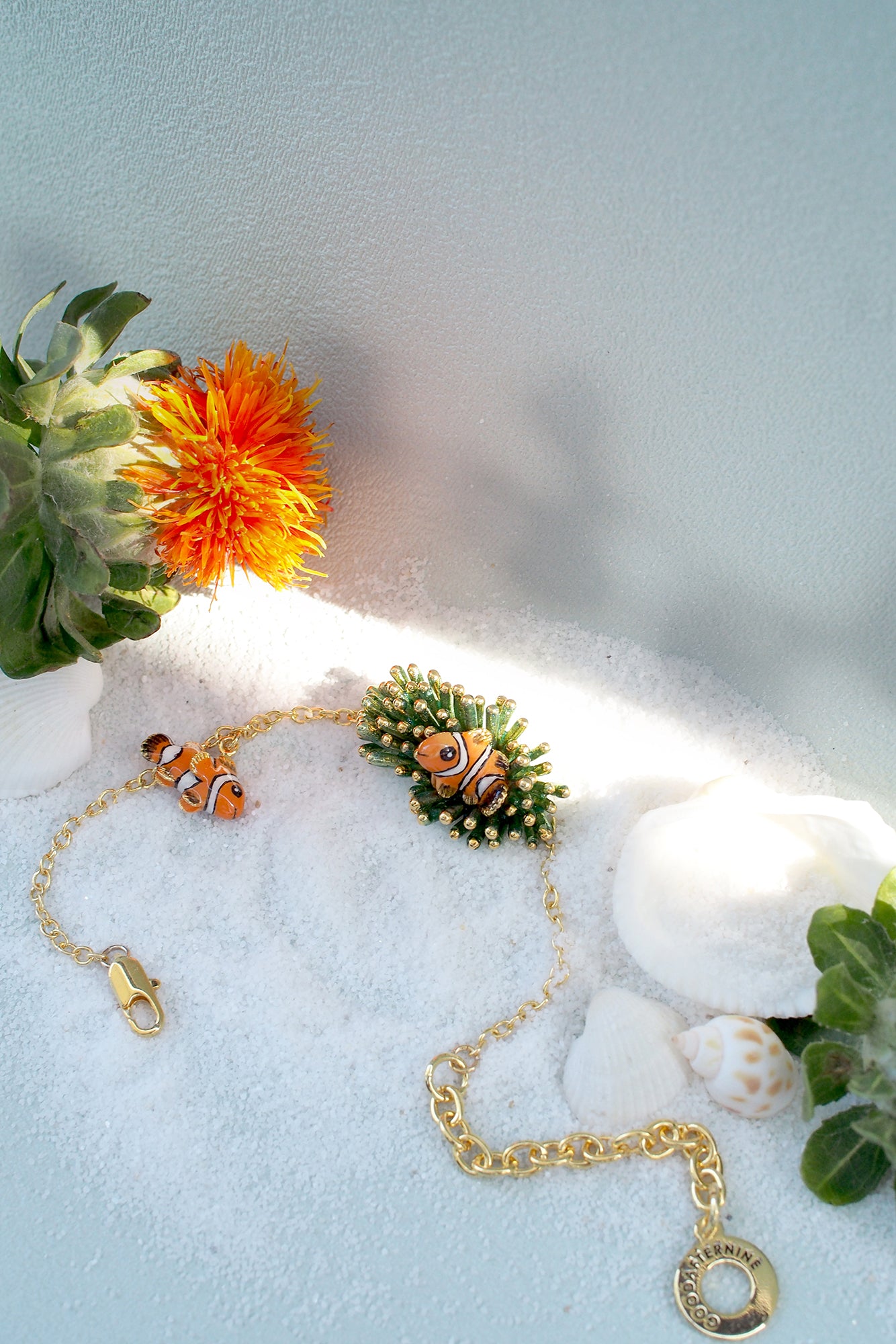  beautiful gold bracelet featuring clownfish and coral design on a sandy beach background.