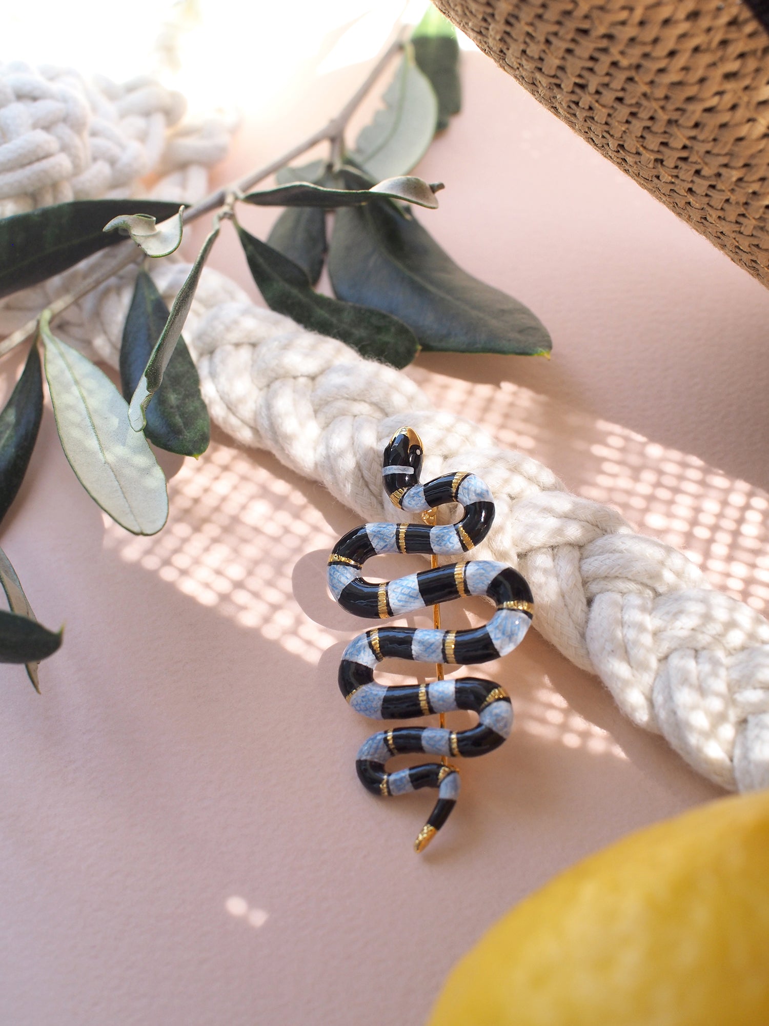 Colorful snake-shaped brooch resting on a white rope next to a lemon and green leaves.