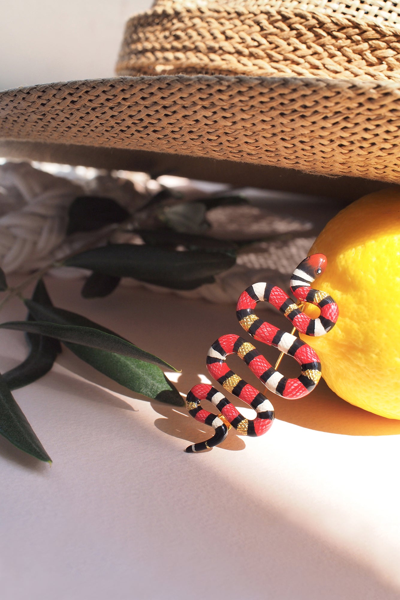 Colorful snake-shaped brooch resting next to a lemon and green leaves.