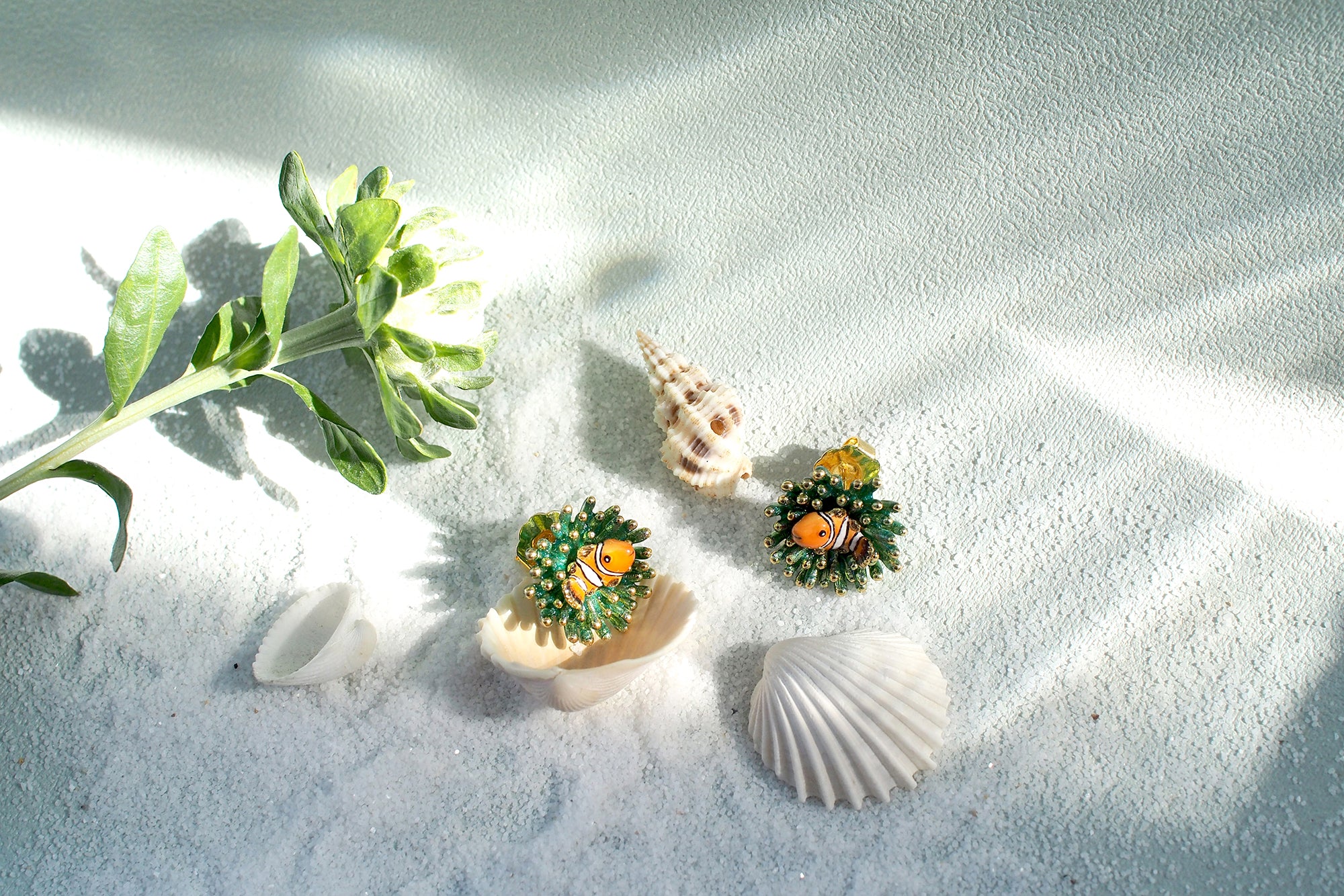 Beautiful ocean-inspired earrings with vibrant clownfish and sea anemone designs on a sandy background.