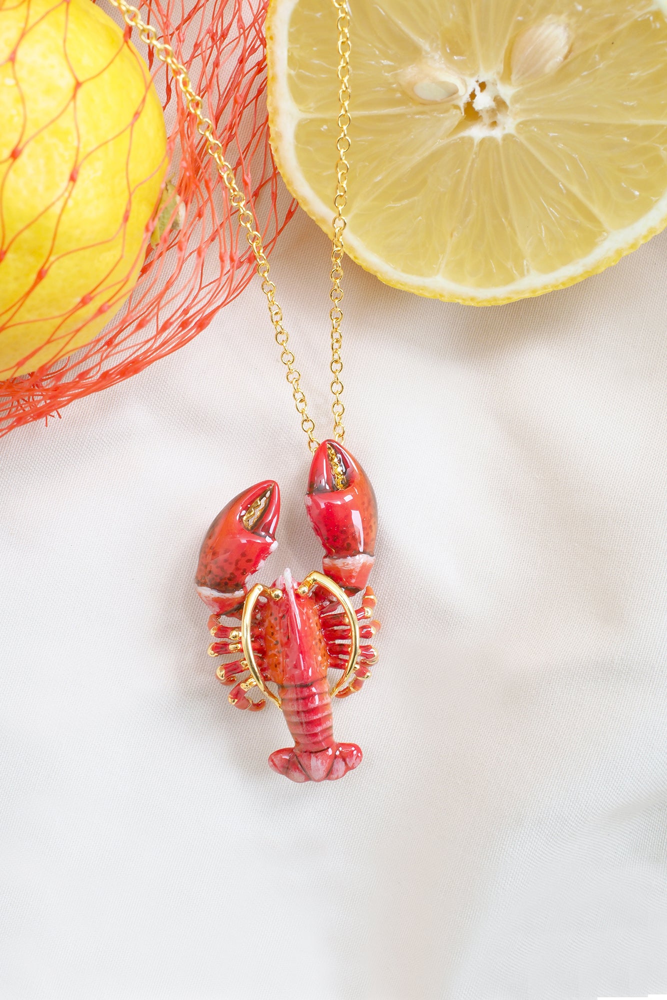 Red lobster-shaped pendant necklace with gold accents on a delicate chain placed on a lemon.