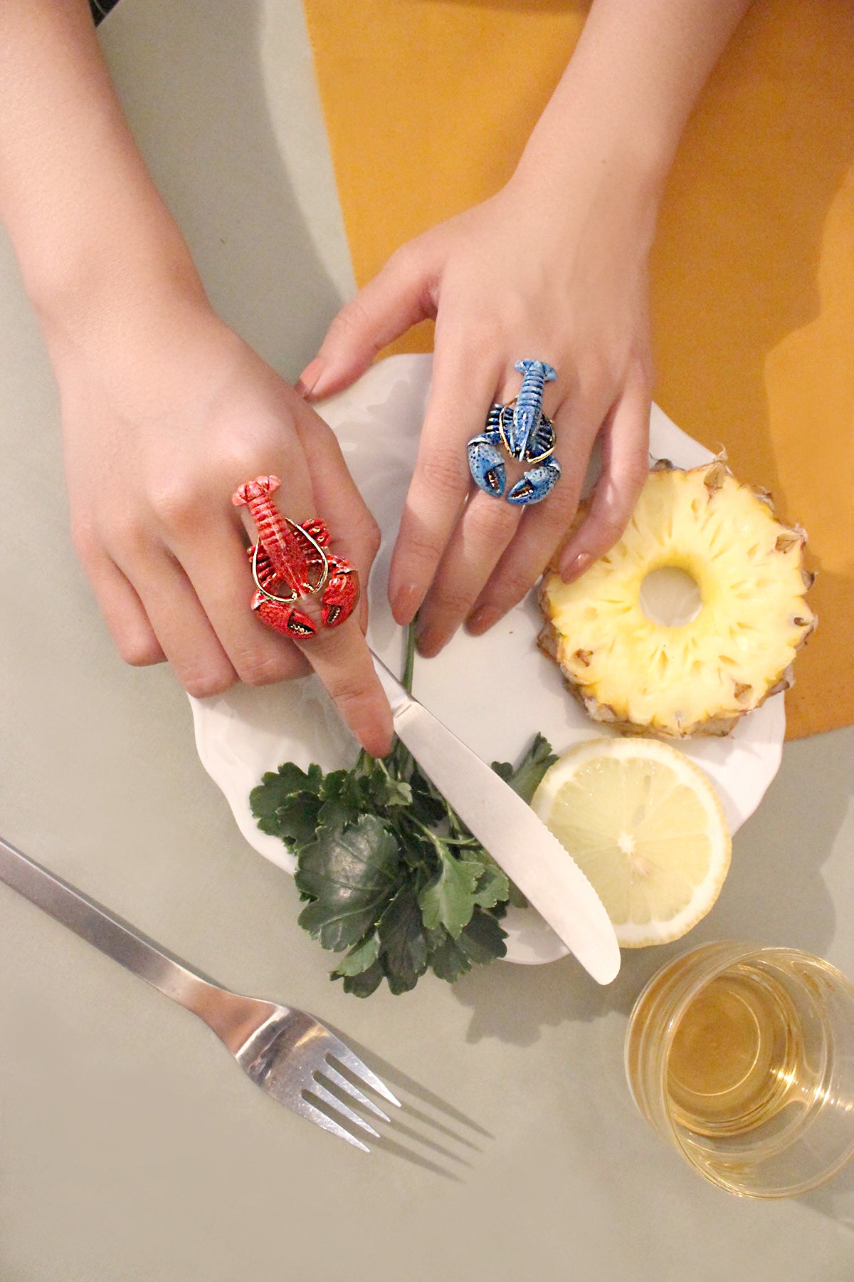 Hands wearing and two unique blue and red lobster rings with the dinning table.