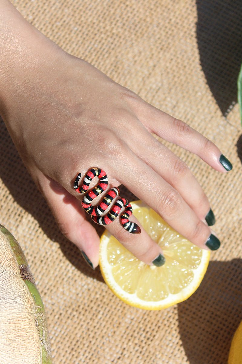 Handcrafted red milk snake ring featuring black and white stripes worn on a person's hand holding a lemon.