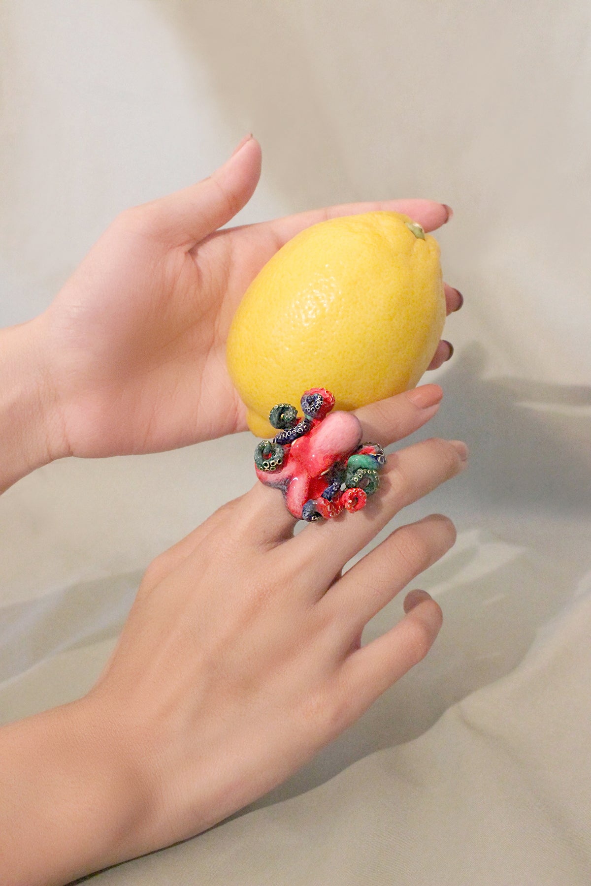 Close-up of a hand with charming red octopus ring holds a lemon.