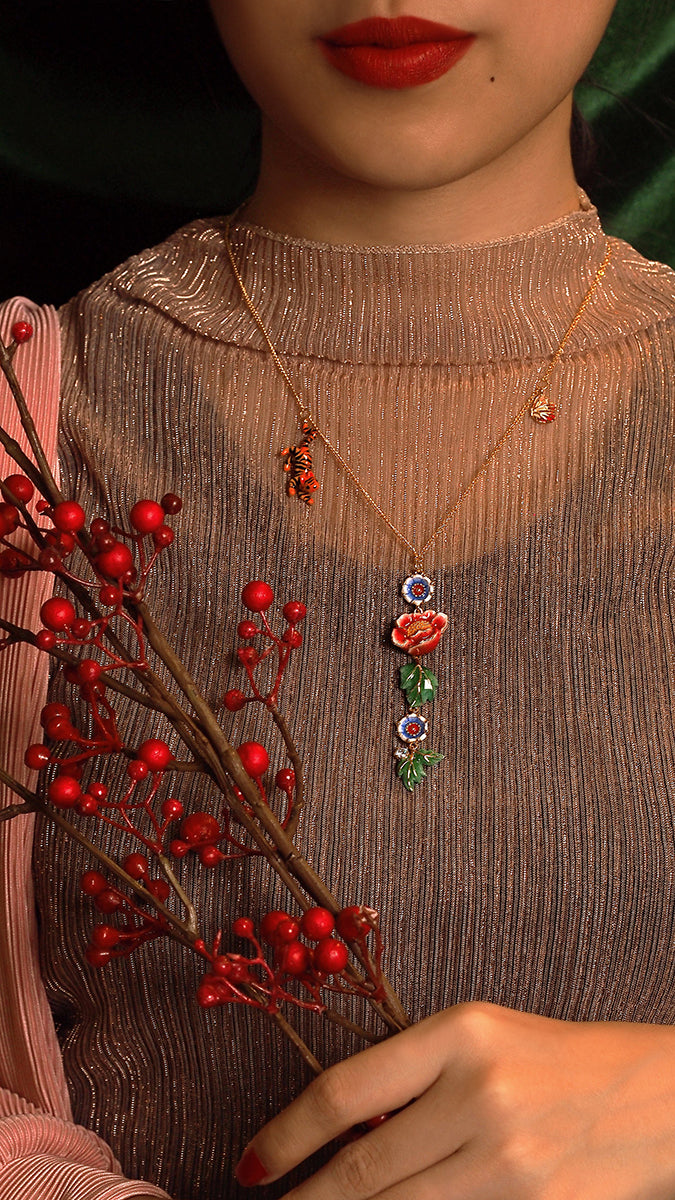 Gold necklaces with floral pendants hang above a model’s deep red lips.