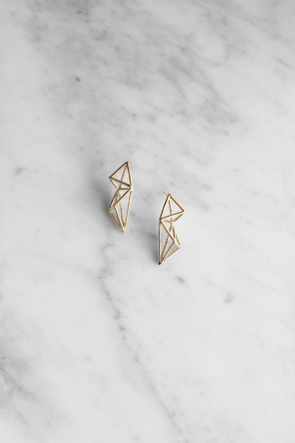 Gold geometric wire earrings with a modern design, placed on a marble background.