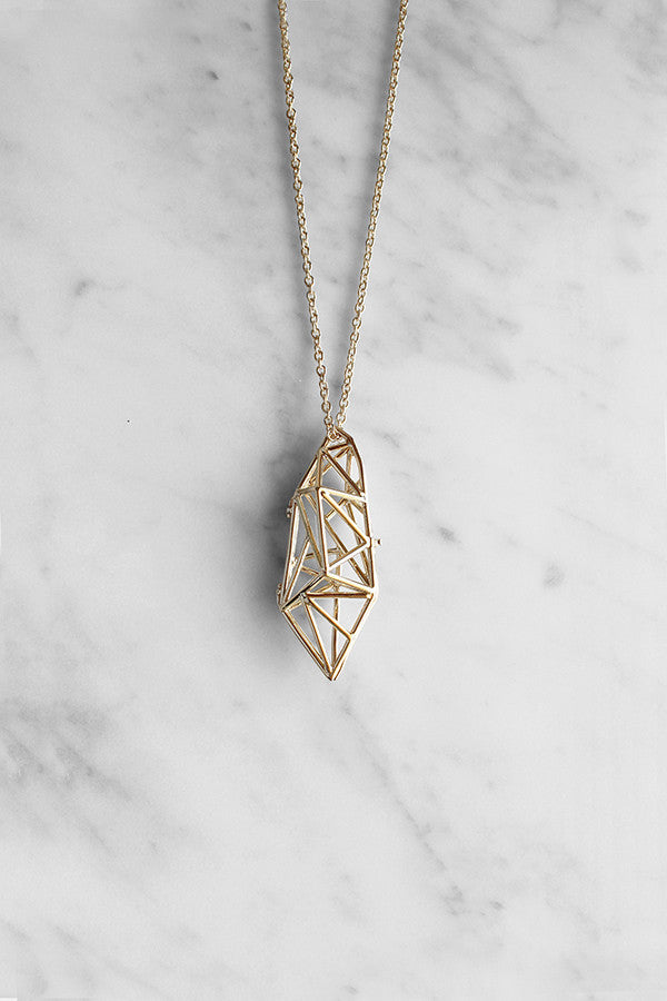 A gold locket necklace featuring a geometric, open lattice design placed on a marble background.