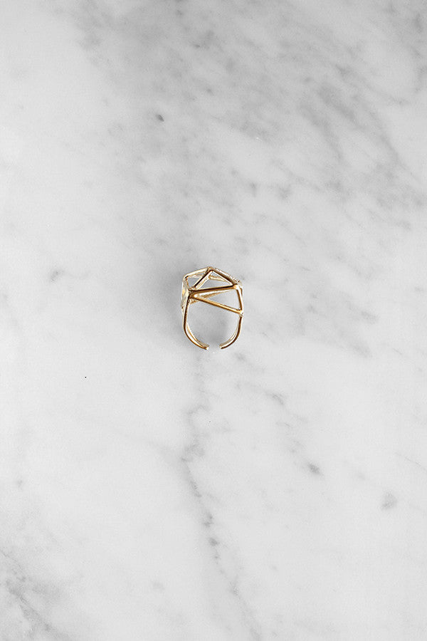 Gold geometric ring with a triangular pattern placed on a marble background.