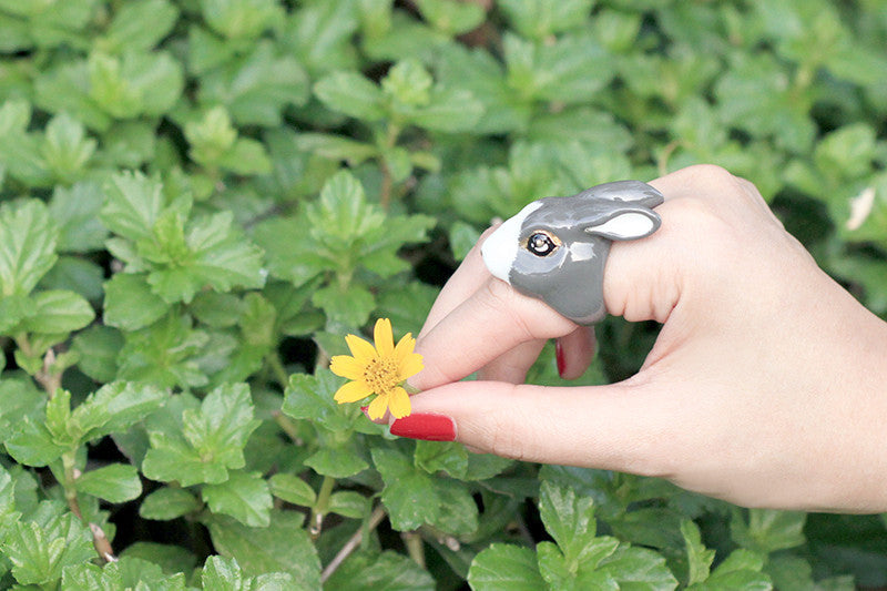 Close-up of a hand wearing a cute rabbit ring gently holding a yellow flower in a green lush.