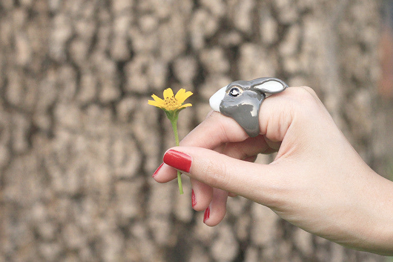 Close-up of a hand with a rabbit ring holding a yellow flower.