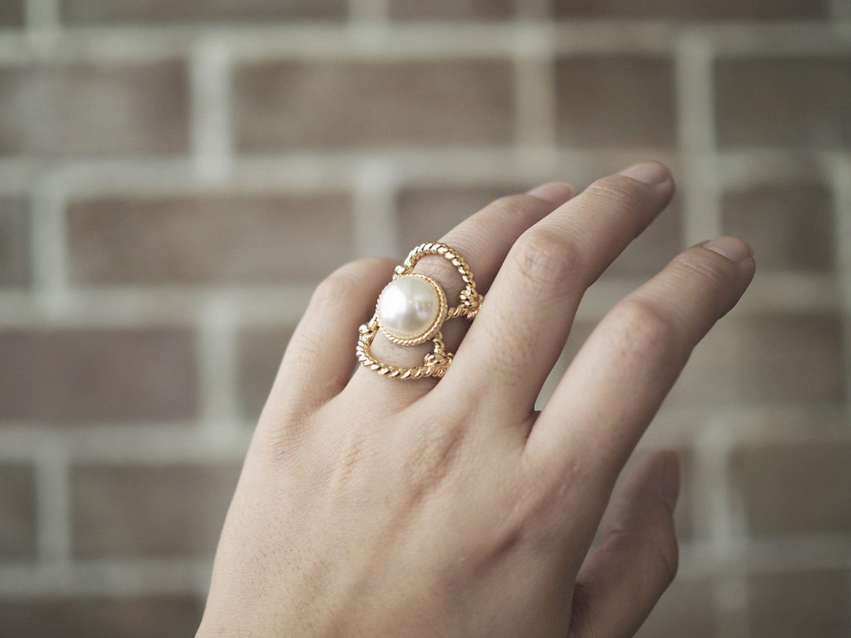 Close-up of a hand adorned with a gold ring with a large costume pearl surrounded by twisted rope design.