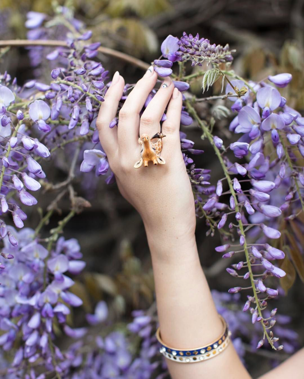 Close-up of a giraffe ring on a hand surrounded by purple flowers.