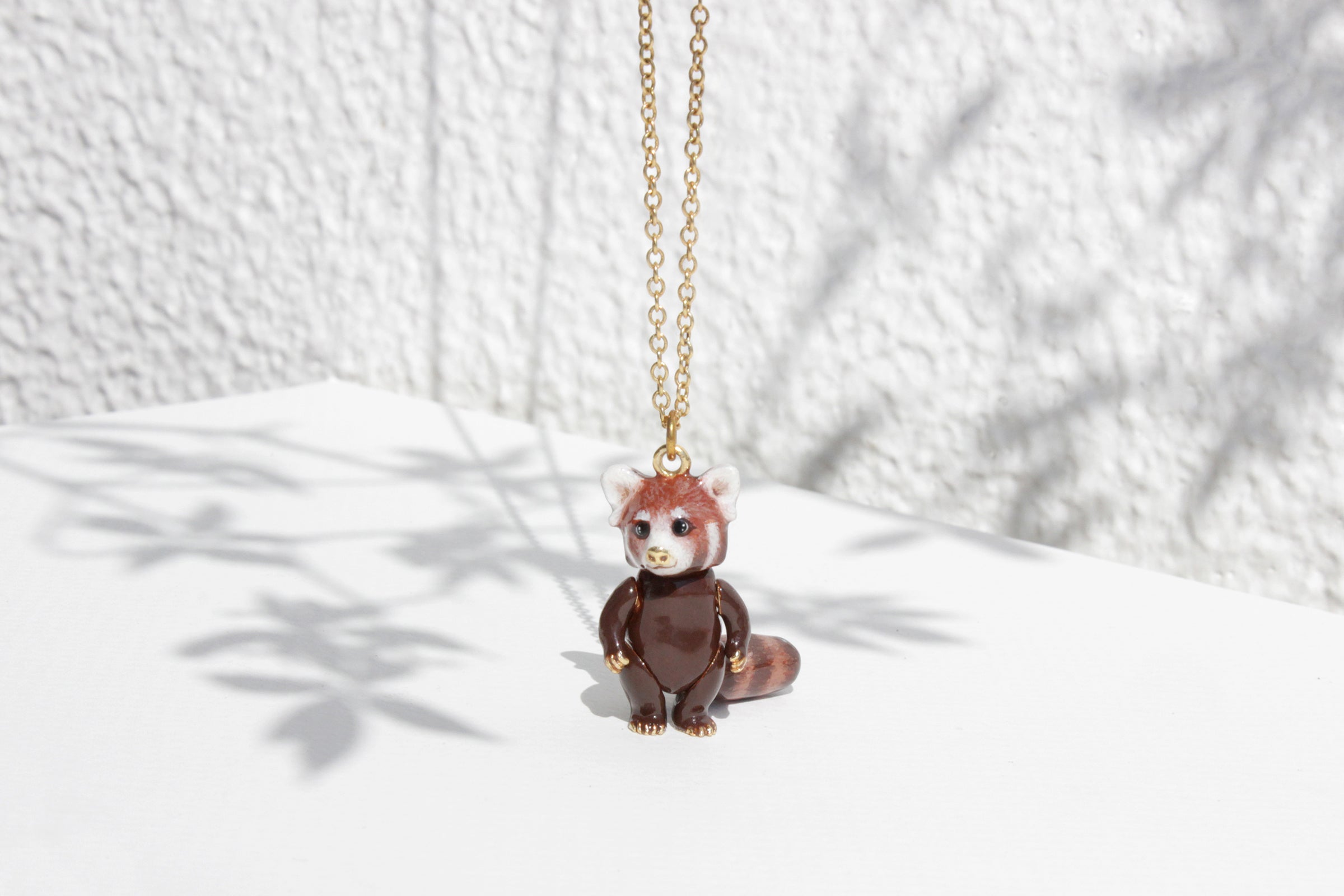 Adorable red panda pendant necklace set in the white background with the shadow of leaves.