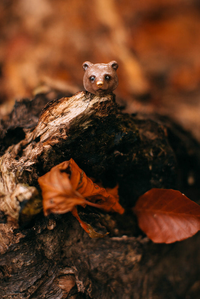 Adorable grizzly bear ring placed on a piece of wood with autumn leaves.