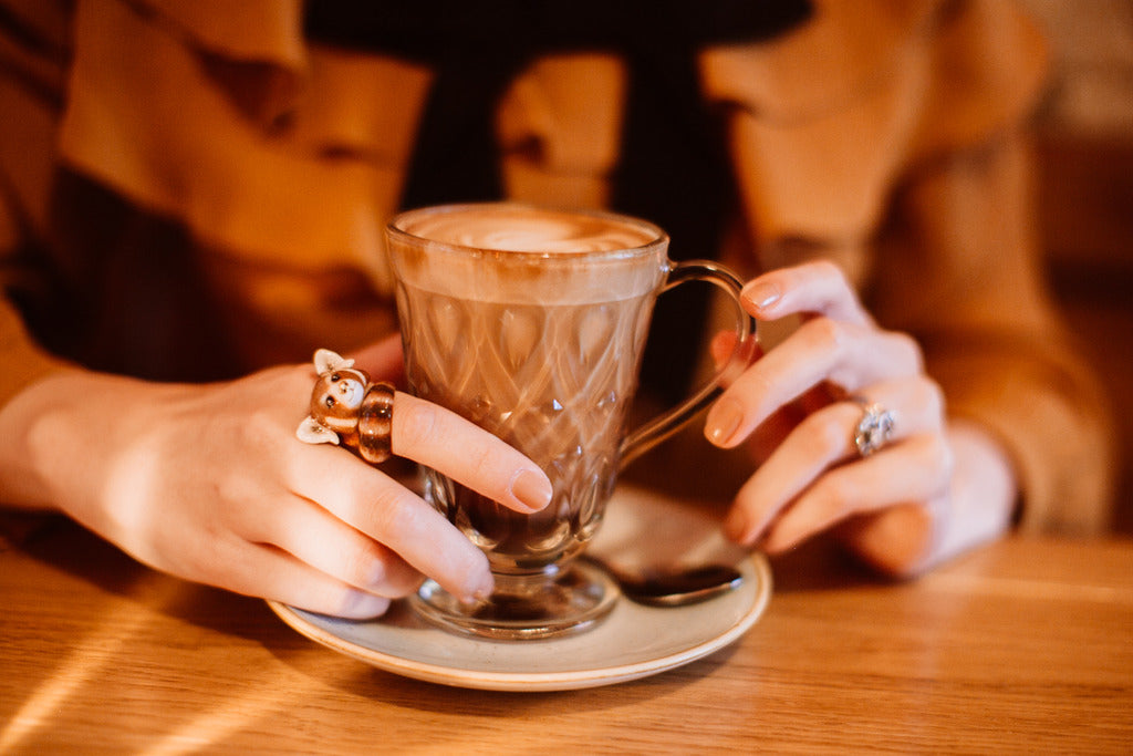 A hand adorned with a charming red panda ring while holding cup of coffee