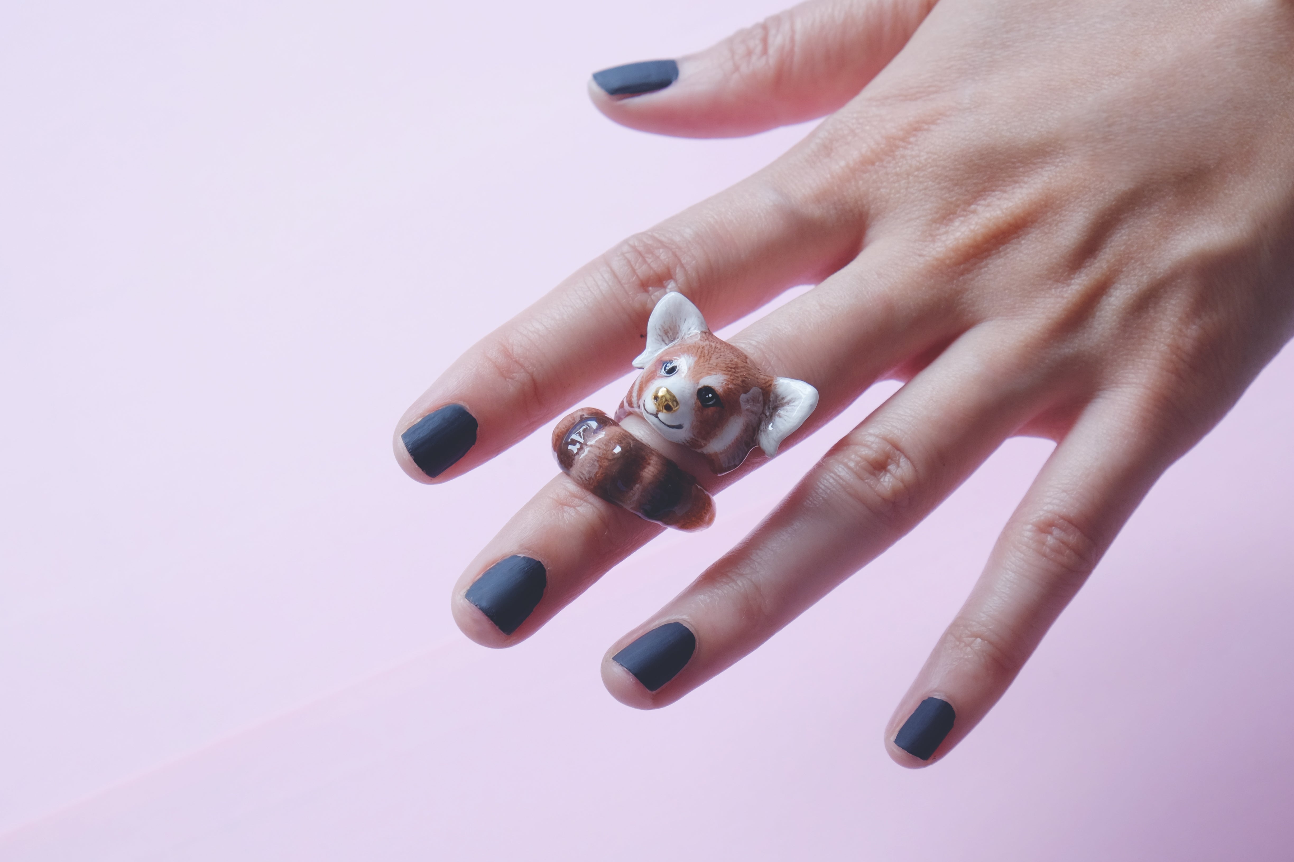 Close-up of a hand with a red panda ring in a light pink background.