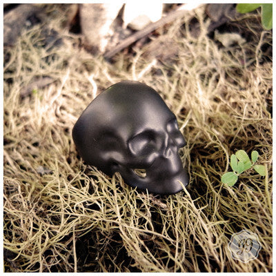 Black skull ring resting amidst natural moss in a forest setting.