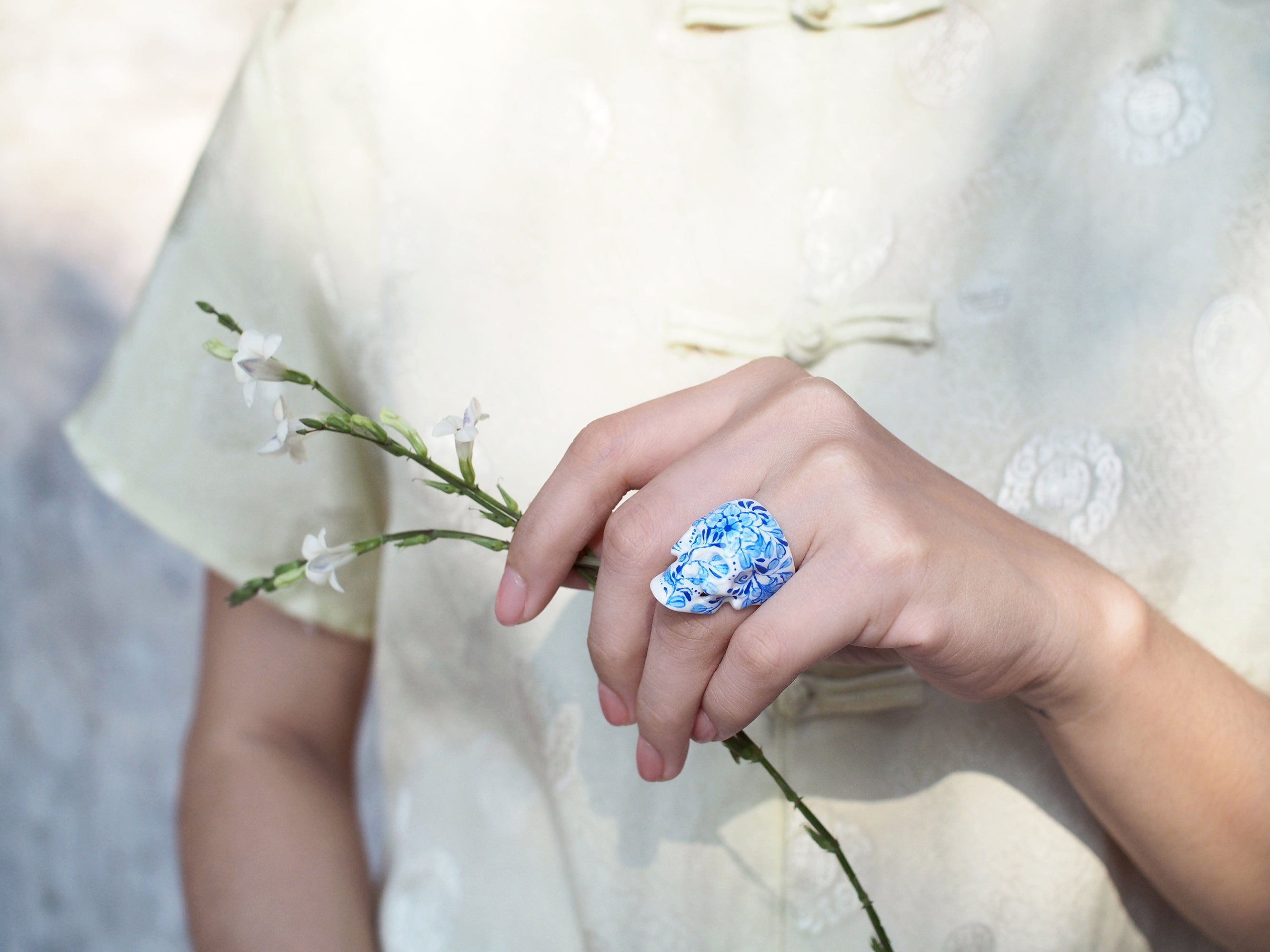 A hand holding a flower while wearing a skull ring with artistic blue floral artwork.