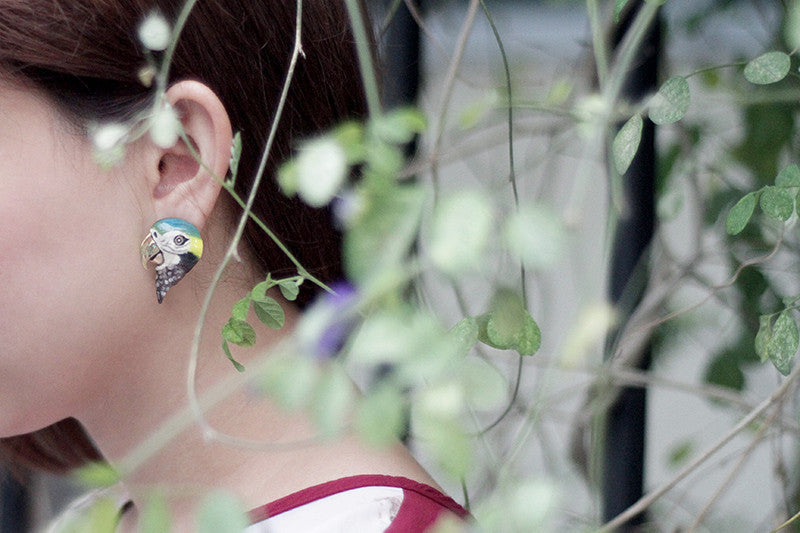 Unique colorful bird earrings worn by a woman, surrounded by natural elements.