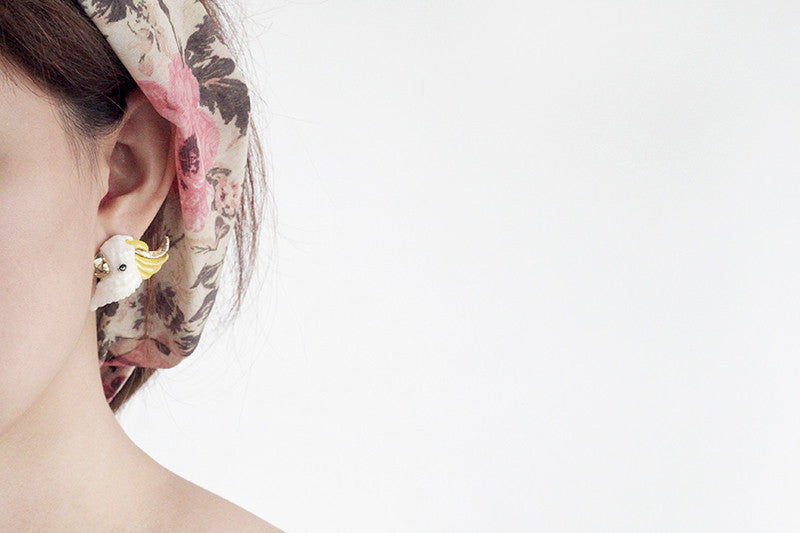 Close-up of a woman wearing adorable cockatoo earrings with floral hair accessories. 