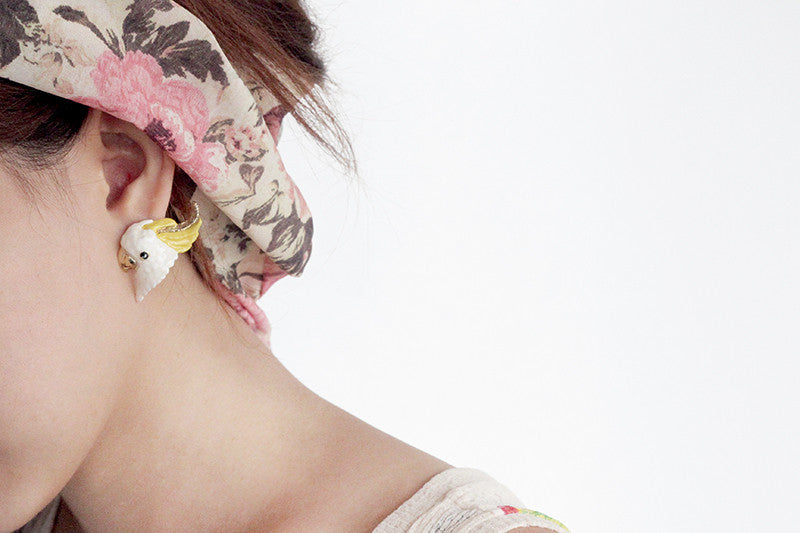 Close-up of a woman wearing adorable cockatoo earrings with floral hair accessories. 