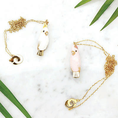 Two nature-inspired whistle necklaces featuring gold chains and cockatoo pendants in white and pink.