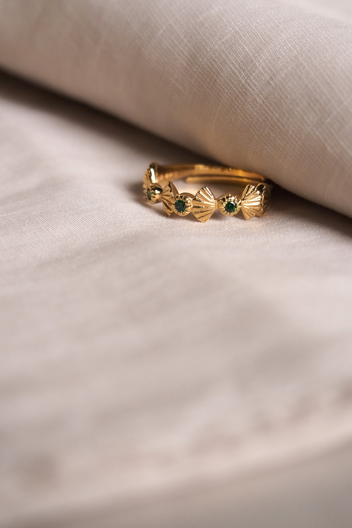 Unique gold ring featuring intricate details and green stones place on fabric.